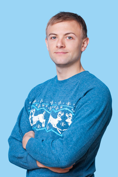 Portrait of young man in sweater with arms crossed against blue background - Фото, изображение