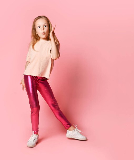 Portrait of shocked young girl in pink leggings looking at camera with mouth - 写真・画像