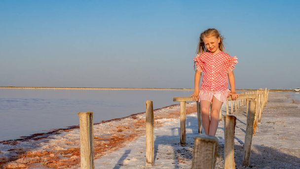 Salt Lake sits a girl on a wooden stick in a red skirt and smiles - 写真・画像
