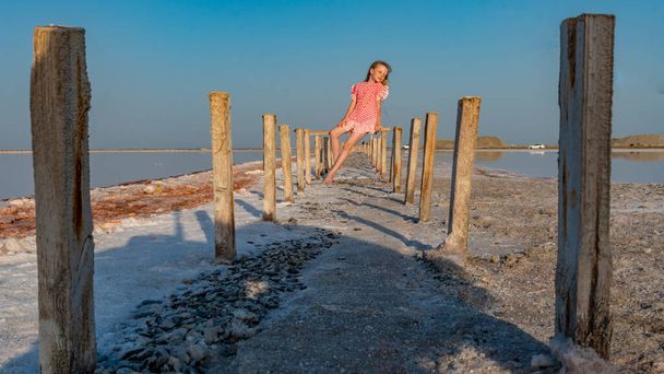 Salt Lake, the girl sitting barefoot in a red dress on wooden sticks, pondered - Zdjęcie, obraz