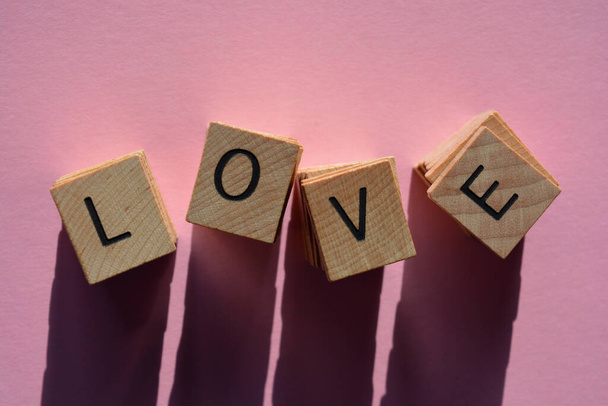 Liebe, Wort in Stapeln von hölzernen Buchstaben aus 3D auf rosa Hintergrund - Foto, Bild