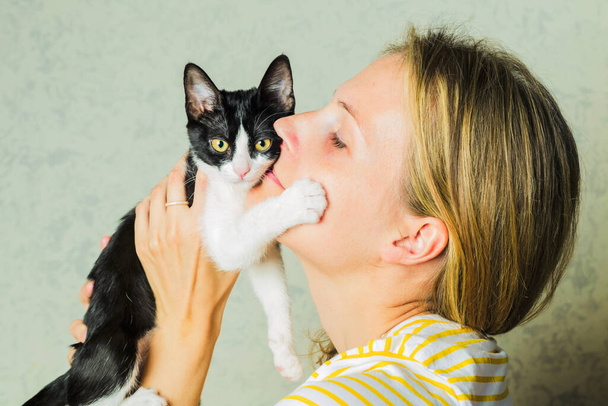 Foto de estilo de vida de una mujer vestida casual que sostiene y acaricia y besa a un gato lindo. gato disfruta estar en niñas brazos. Enfoque selectivo
. - Foto, Imagen