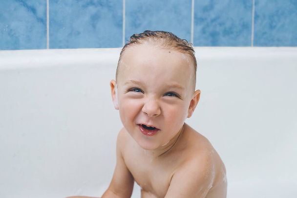 Grappige emotionele peuter zit in de badkamer. het kind maakt een grappige ontevreden grimas - Foto, afbeelding