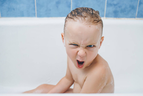 Bebé emocional muecas mientras se lava en el baño con espuma. sobre hace una mueca malvada descontenta
 - Foto, Imagen