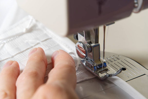 Una mujer trabaja en una máquina de coser. costurera cose cortinas blancas, vista de cerca
. - Foto, Imagen