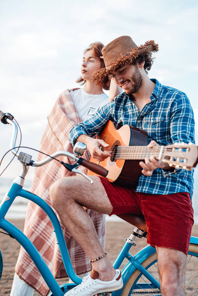 男の子は青い自転車でギターを弾いている。少女は彼の後ろに立っている - 写真・画像