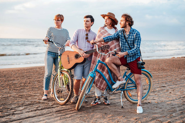 Friends with the guitar on the beach with their bicycles - Zdjęcie, obraz