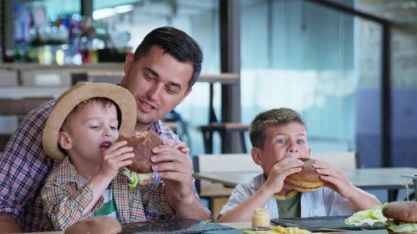 niños comen, feliz alegre padre varón junto con sus hijos hambrientos disfruta comiendo sabrosas hamburguesas d
 - Metraje, vídeo