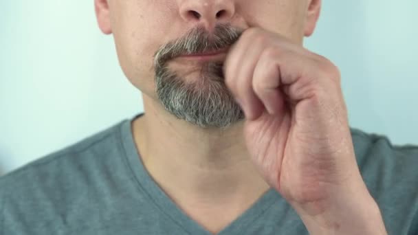 Een man van middelbare leeftijd veegt zijn snor af na het eten met zijn hand, close-up, 4K - Video
