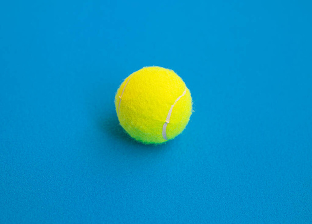Single yellow tennis ball isolated on blue background. - Foto, afbeelding