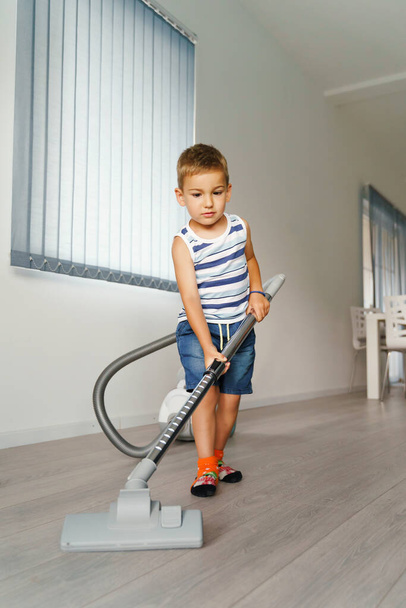 Kleines Kind benutzt Staubsauger zu Hause - Kleiner Junge putzt Fußboden in Wohnung - Kind macht Hausarbeit mit Spaß - Frontansicht im Sommertag in voller Länge - Entwicklung der Kindheit echte Menschen Konzept - Foto, Bild