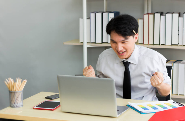The male employee expressed satisfaction that he had finished his work. Asian man is excited while looking at a laptop. - Photo, image