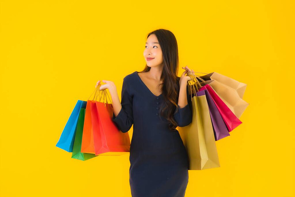 Retrato hermosa joven mujer asiática con colorido bolso de compras sobre fondo aislado amarillo - Foto, Imagen