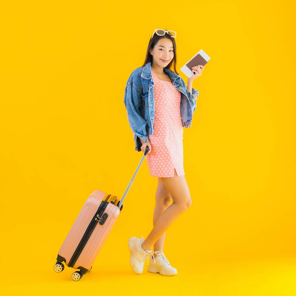 Portré gyönyörű fiatal ázsiai nő poggyász utazási táska útlevél és beszállókártya jegy sárga elszigetelt háttér - Fotó, kép