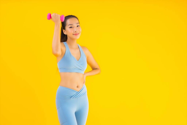 Retrato hermosa joven asiática mujer con mancuerna y ropa deportiva listo para el ejercicio en amarillo aislado fondo
 - Foto, Imagen
