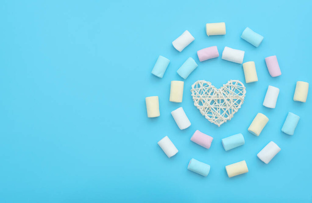 White rattan heart and delicious marshmallows on blue background. Happy day, breakfast, love, good morning concepts. Valentine greeting card. Flat lay style. - Foto, imagen