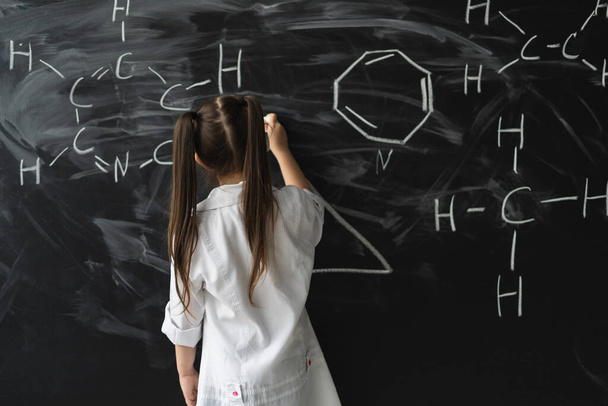 Cute little girl writing on a blackboard at a chemistry lesson in class. White coat and goggles. Place for text - Photo, image