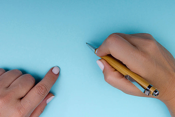 Pen in female hands on a blue background - 写真・画像
