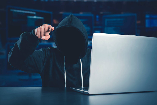 Dangerous hacker threatening by pointing at the camera with laptop and coding background - Foto, Bild