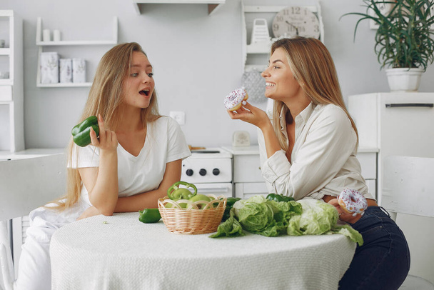 Beautiful and sporty girls in a kitchen with a vegetables - Foto, Bild