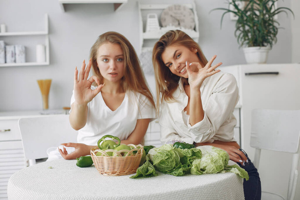 Beautiful and sporty girls in a kitchen with a vegetables - Фото, зображення