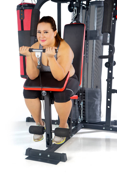 Obesity woman exercising her biceps with a fitness machine in the studio, isolated on white background - Foto, imagen