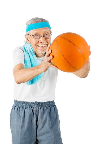 Old man playing and passing a basketball in the studio while wearing sportswear. Isolated on white background - Photo, image