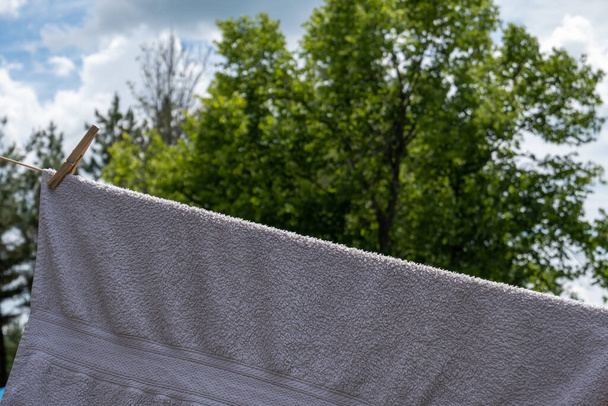A white towel is affixed to a clothesline with a wooden clothespin and is hanging outside to dry. - Photo, Image