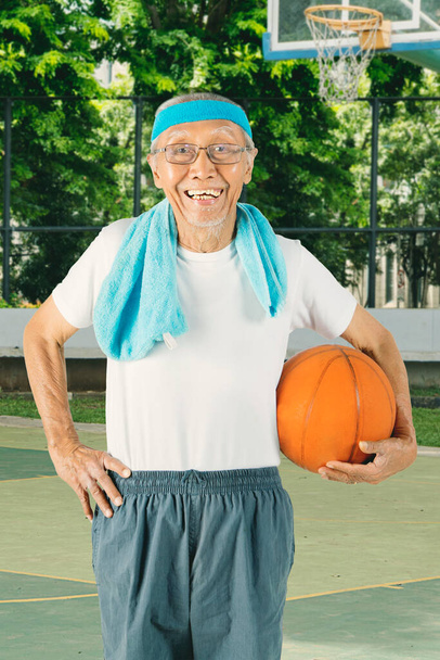 Senior trägt Sportbekleidung, während er einen Basketball hält und auf dem Feld steht - Foto, Bild