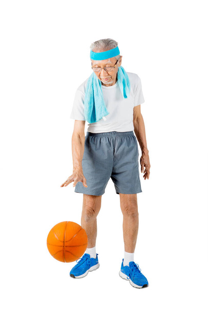 Senior man wearing sportswear while playing a basketball in the studio. Isolated on white background - 写真・画像