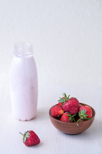 Czerwone truskawki w glinianym kubku i jogurt w butelce na stole, śniadanie letnie - Zdjęcie, obraz