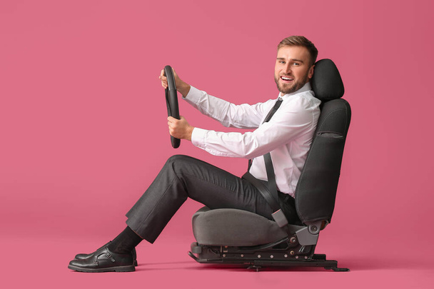 Jovem empresário com volante sentado no assento do carro contra fundo de cor
 - Foto, Imagem