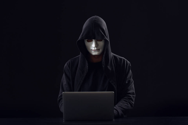 Professional hacker using laptop at table against dark background - Foto, afbeelding