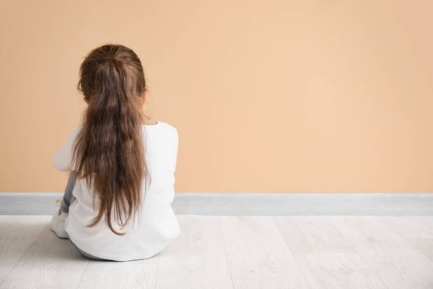 Triste petite fille avec trouble autistique assis près du mur de couleur, vue de dos - Photo, image