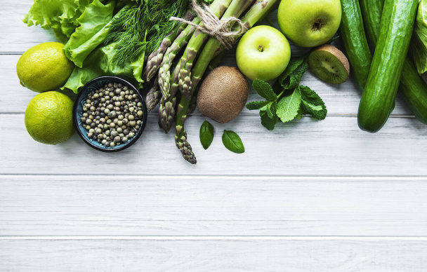 Zdravé vegetariánské jídlo koncept pozadí, čerstvé zelené jídlo výběr pro detox stravy, jablko, okurka, chřest, avokádo, vápno, salát pohled shora na bílém dřevěném pozadí - Fotografie, Obrázek
