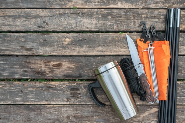Stainless cup, knife, parts of tent and rope on the wooden table background with copy space. - Фото, зображення