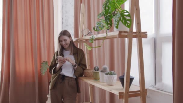 Attractive woman uses phone near the shelf with flowers - Кадри, відео