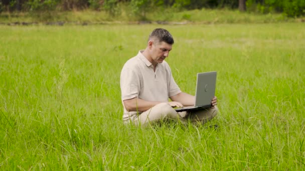 Freiberufler nutzt Laptop für Fernarbeit auf dem Rasen im Gras - Filmmaterial, Video