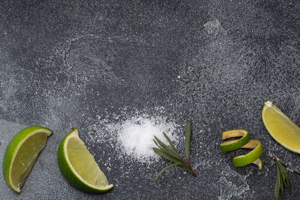 Slices of fresh lime, salt and rosemary dark concrete background. Copy space. Ingredients for making a tequila cocktail. - Foto, Imagen