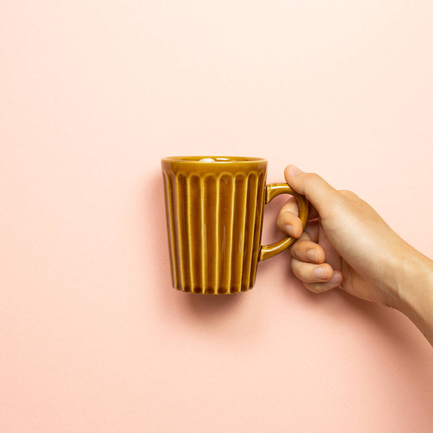 Female hand holding brown empty mug cup on pink background - Foto, imagen