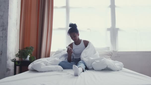 かなり若いアフリカ系アメリカ人女性はベッドでリラックスしながら電話を使用します - 映像、動画