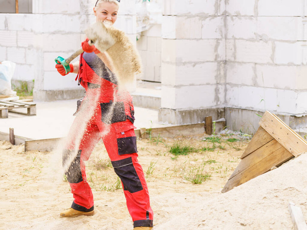 Mulher trabalhando duro no canteiro de obras, usando pá cavando solo de areia. Construído parcialmente novo estágio inicial da casa. Indústria. - Foto, Imagem