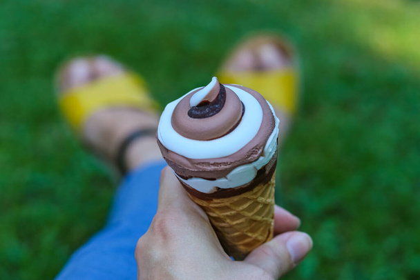 Creamy chocolate ice cream cone in hand on green grass background - Photo, Image