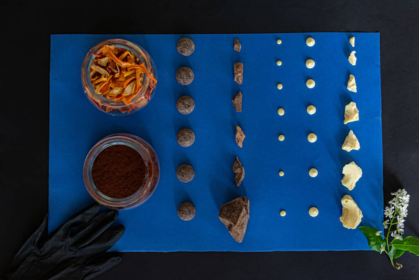 Vista superior de trozos de chocolate sobre un fondo azul y negro y una ramita de flores blancas de primavera, cacao en polvo en un frasco de vidrio y cáscaras de naranja para frutas confitadas
 - Foto, imagen