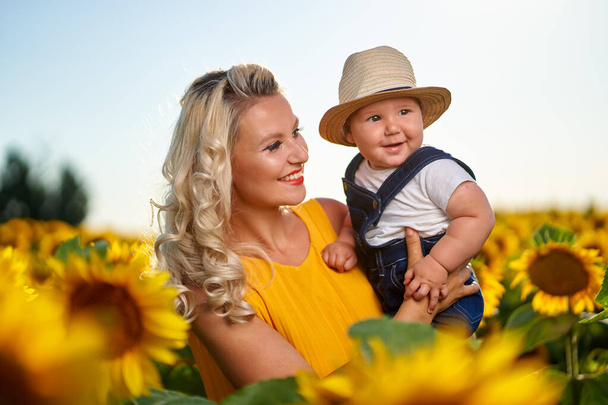 Young mother with her baby boy in a sunflower field - Photo, image