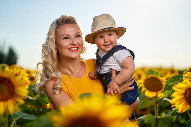 Young mother with her baby boy in a sunflower field - Фото, зображення