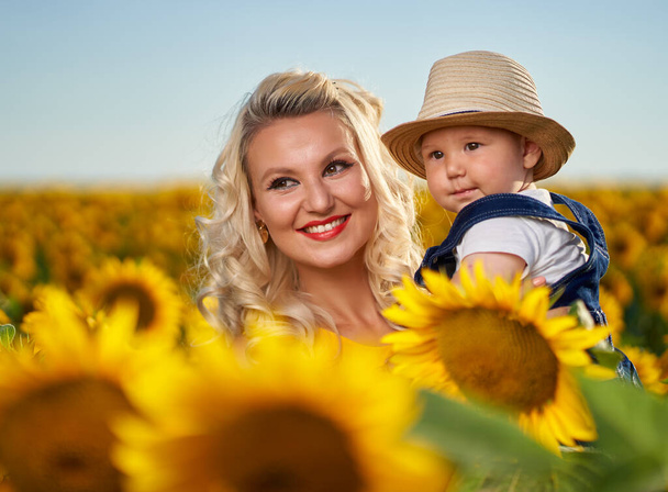Young mother with her baby boy in a sunflower field - Фото, зображення