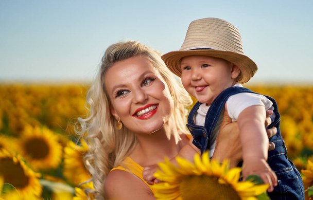 Young mother with her baby boy in a sunflower field - Fotoğraf, Görsel