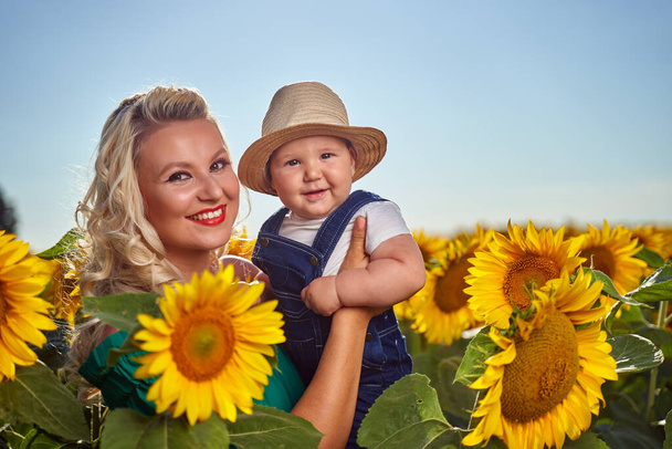 Young mother with her baby boy in a sunflower field - 写真・画像