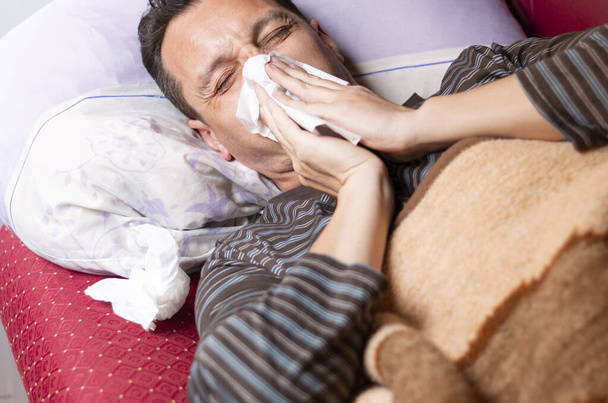 Man blowing his nose while lying sick in bed - Photo, Image